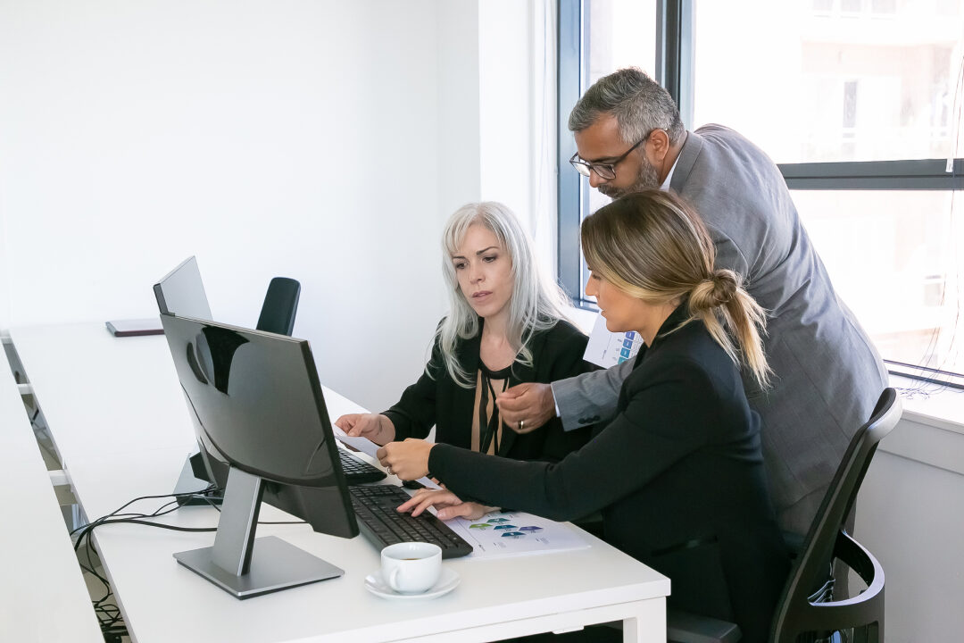 business-team-three-analyzing-reports-sitting-workplace-with-monitors-together-holding-reviewing-discussing-papers-with-charts-copy-space-inclusive-workplace-concept