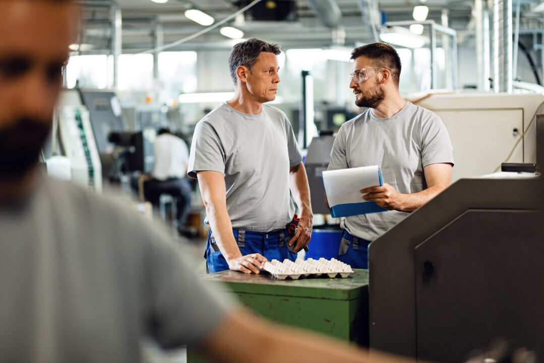 male-coworkers-communicating-while-going-though-paperwork-factory 1