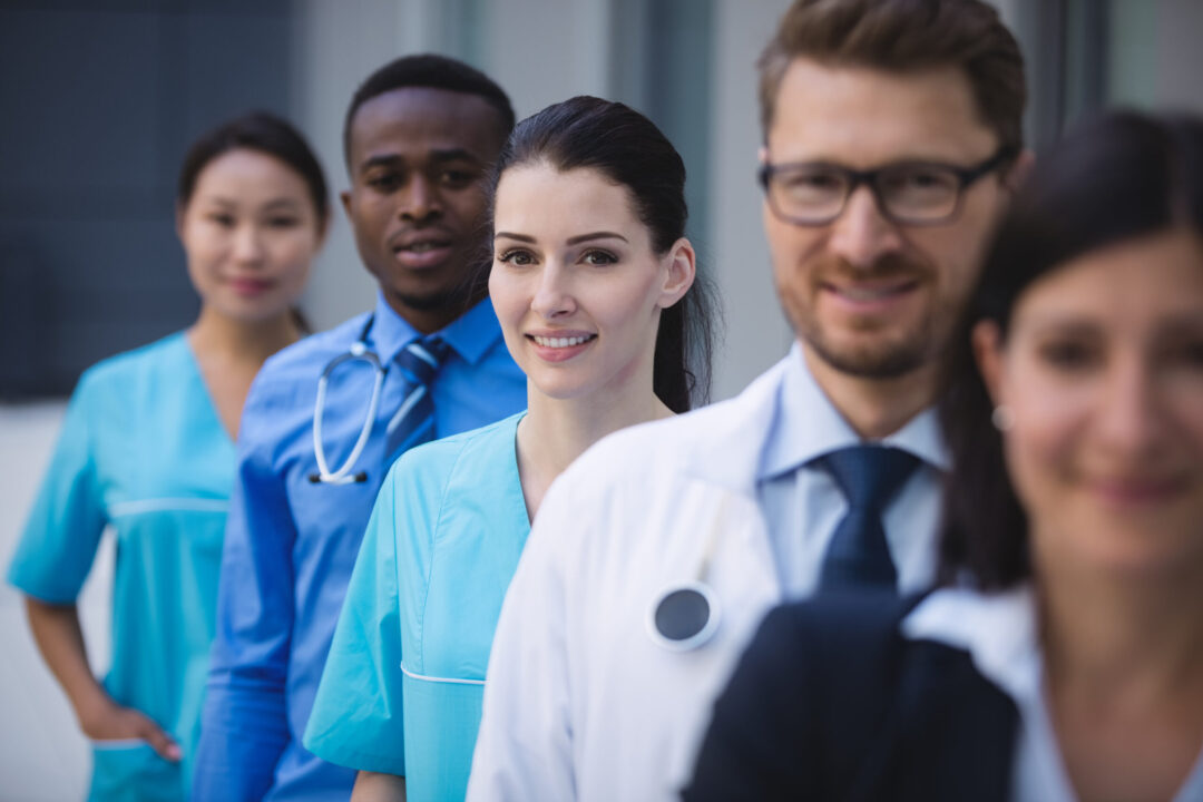 Portrait of smiling doctors standing in row at hospital premises